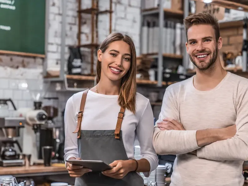 Smiling café owners standing behind the counter holding a tablet in a modern coffee shop Business directory